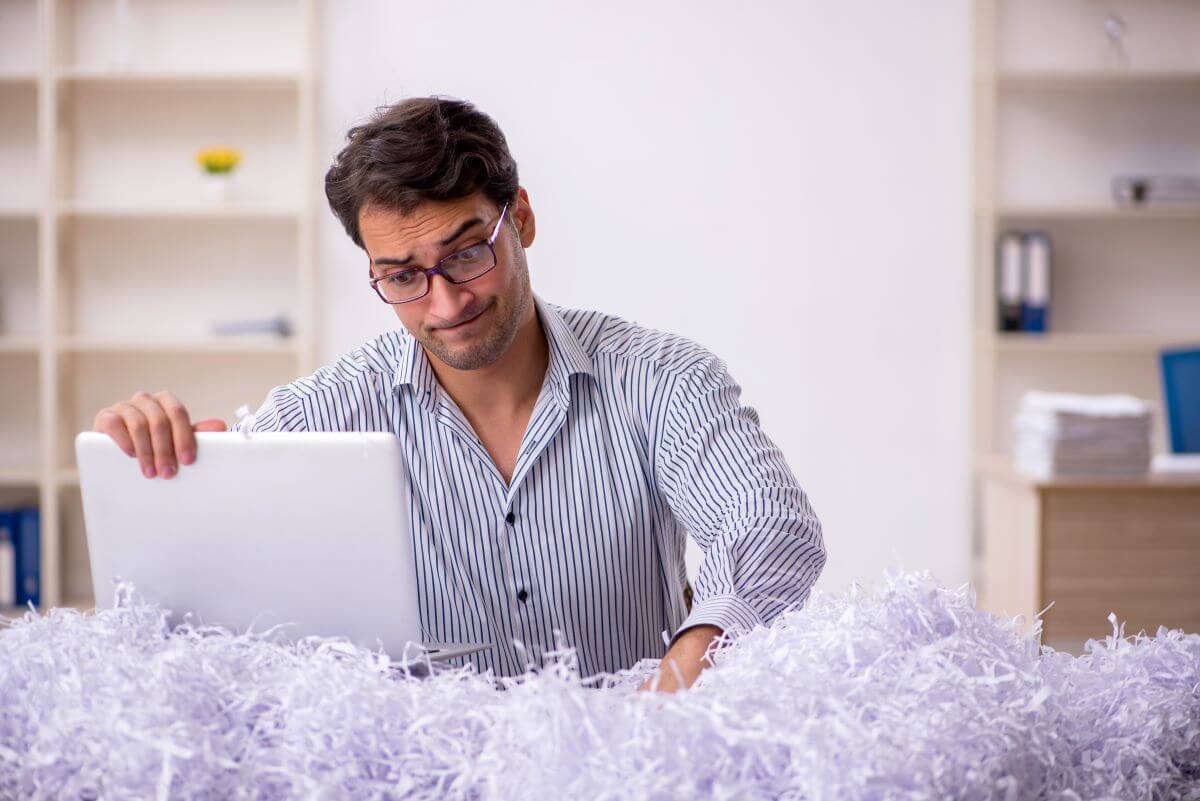 Man looking at computer upset with document shredding paper around him