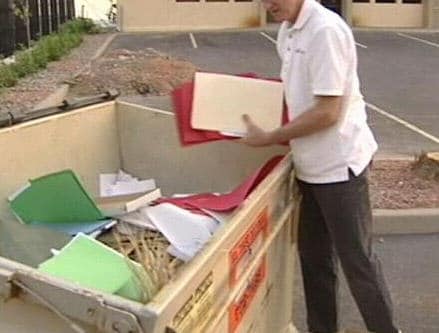 A man retrieving sensitive documents from within a dumpster