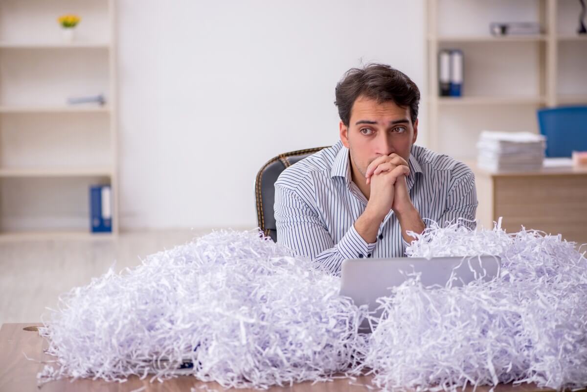 Man in office looking at computer upset with document shredding paper around him