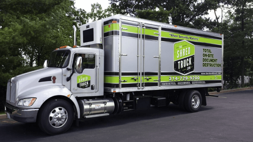 A large white and green shred truck is parked on a road. It features company branding and the tagline "Total On-Site Document Destruction" on its side.